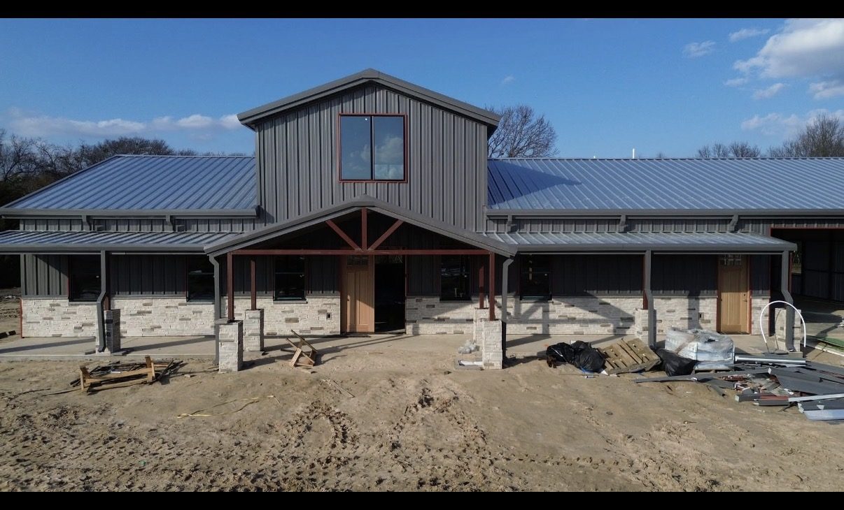 Custom barndominium with metal roof, masonry wainscot and covered porch by Double B Builders